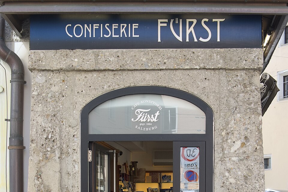 薩爾斯堡老街上一間店面的入口，門楣上方有深藍底白字的 CONFISERIE FÜRST 招牌，門內可見商品櫃。